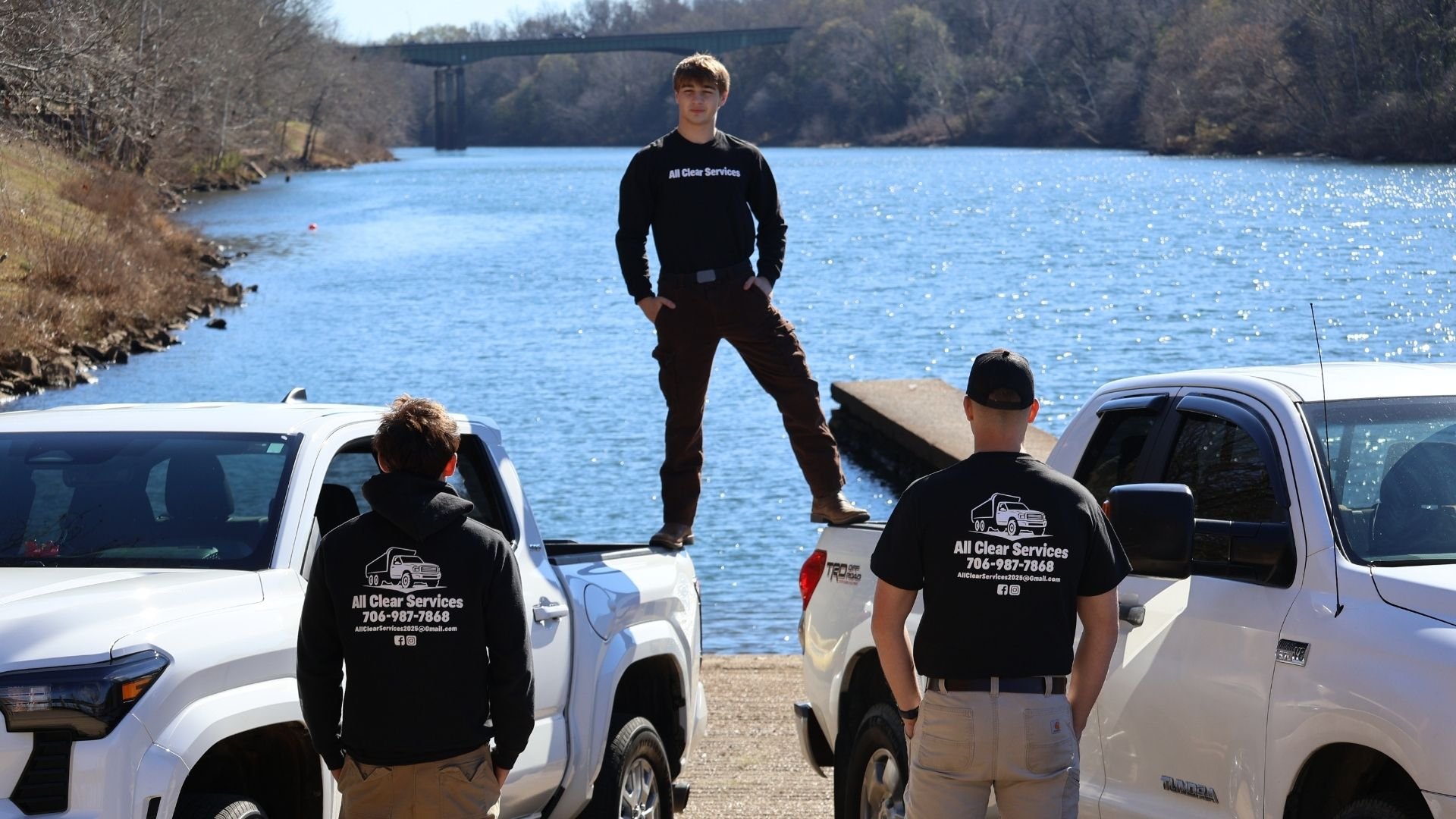 Moving workers standing near trucks by river, one balanced on truck roof