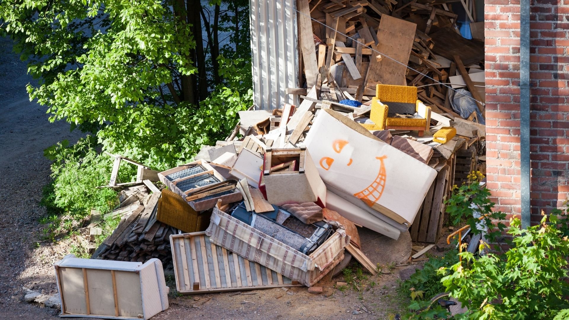 Moving day debris and discarded furniture piled near brick wall and trees