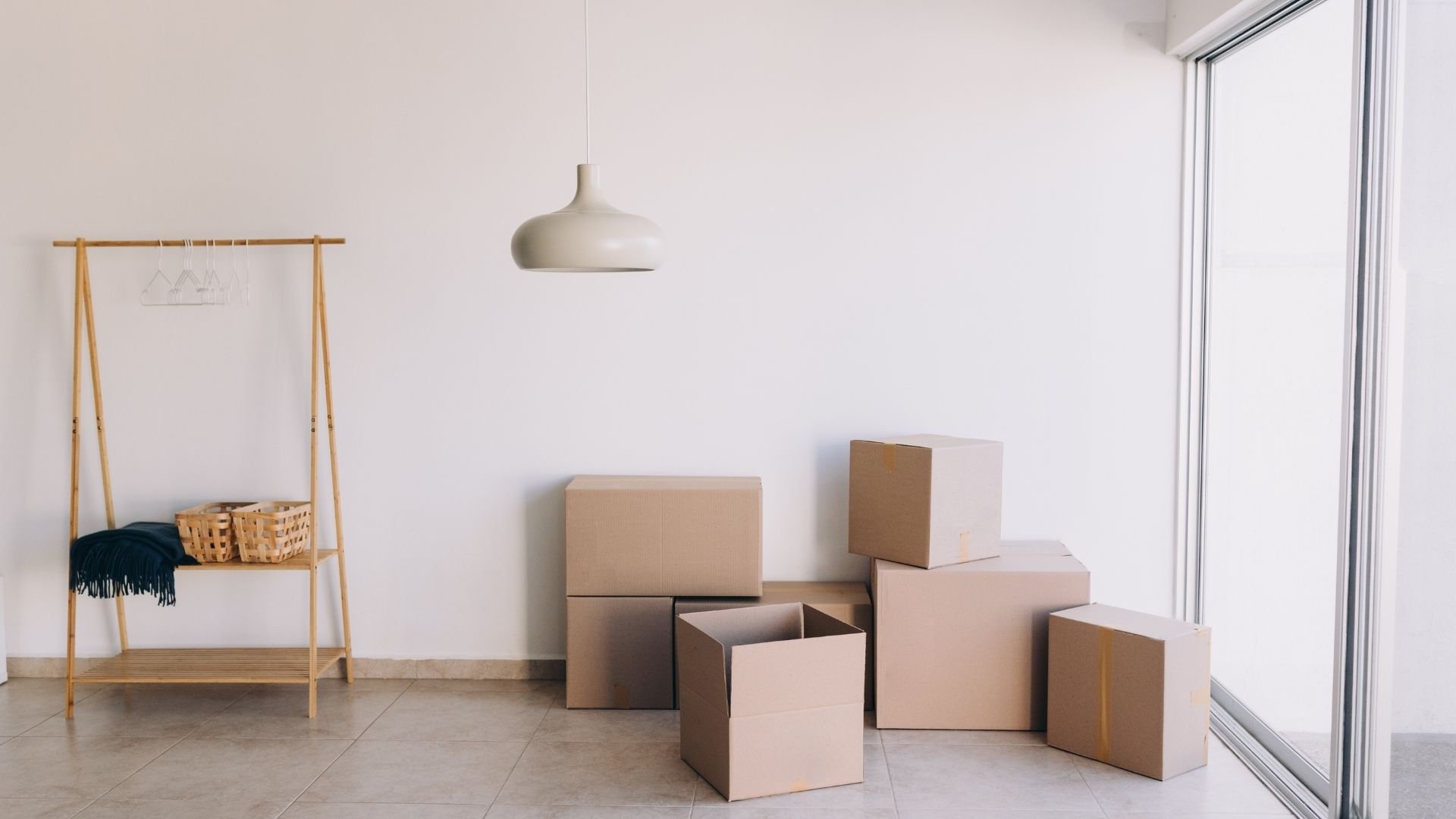 Moving boxes stacked in minimalist room with wooden rack and pendant lamp